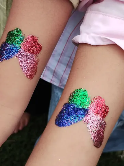 A pair of matching abstract butterfly tattoos. The blend of green, blue, red, and pink glitter makes these designs bright and cheerful.