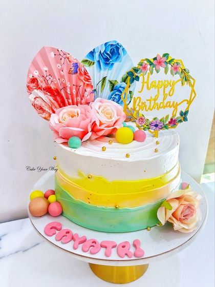 A cake as bright and beautiful as the celebration itself, with a colorful striped design, fresh flowers, and decorative fans.