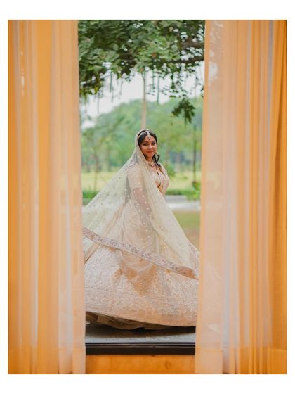 A bride twirls in her golden lehenga, seen through a window, creating a beautiful and dreamy effect.