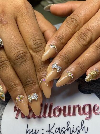 A fun and glamorous set with a nude base, gold glitter, and sparkling 3D rhinestone bow charms.