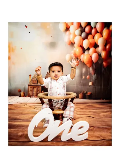 A whimsical first birthday photo with a baby sitting in front of a large 'ONE' sign, with a backdrop suggesting he's floating with balloons.