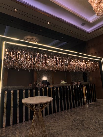 A chic and modern bar setup with a black and white striped front and a canopy of hanging crystal chandeliers, perfect for a sophisticated cocktail event.