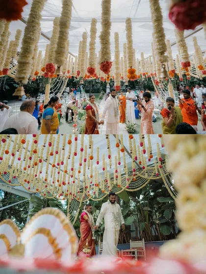 A breathtaking view of a wedding ceremony under a transparent tent. The mandap is a cascade of white and orange floral garlands, creating a vibrant and sacred space surrounded by nature.