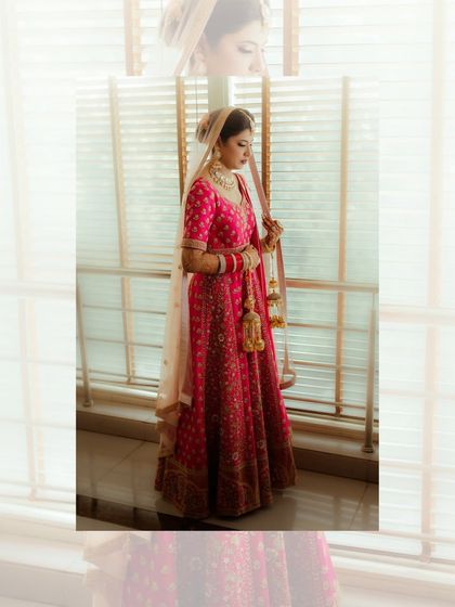 A full-length portrait of Simran, her pink lehenga beautifully captured as she stands by a window.