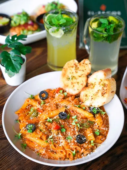 A hearty bowl of penne pasta in a red sauce, served with garlic bread and mojitos. This shot captures a complete and satisfying cafe meal in a bright, inviting setting.