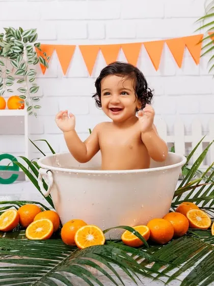 Pure joy! A baby boy laughs and splashes in the tub during his orange-themed first birthday shoot.