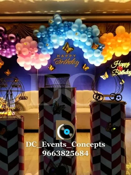 A whimsical butterfly-themed birthday party setup. The multi-colored balloon arch and decorative props like miniature ferris wheels create a magical and playful atmosphere.