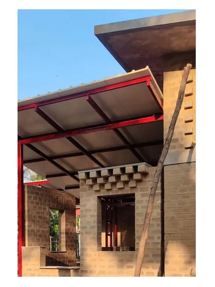 A close-up of the building's corner during construction, showing the interplay between the mud brick walls, the concrete slab, and the steel frame for the roof.