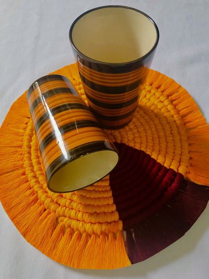 This vibrant orange and maroon mat is being used as a coaster for a set of glasses. It’s a great way to protect your surfaces while adding a splash of color and handmade texture.