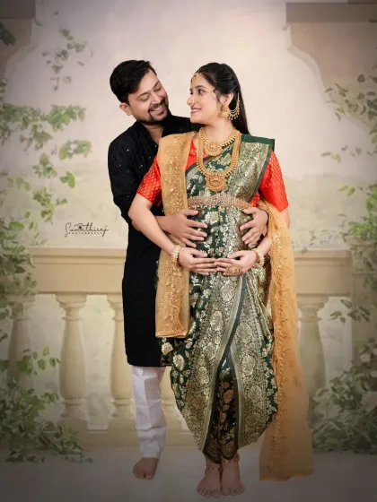 An intimate couple portrait in traditional attire. The husband gently holds his wife's baby bump, creating a moment of connection and love against a classic backdrop.