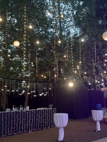 A stylish outdoor bar setup for a reception. The area is defined by a curtain of hanging lights and candles, creating a cool and sophisticated spot for guests to grab a drink.