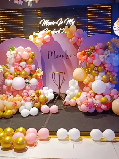 A beautiful stage decoration with arched backdrops and organic balloon garlands for a 'Mom Love' themed event.