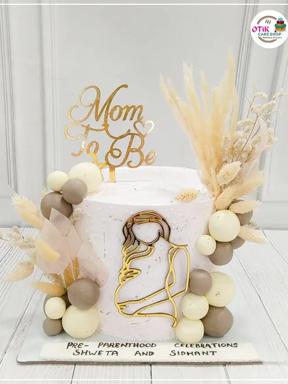 We create beautiful cakes to celebrate new beginnings. This 'Mom-to-Be' cake features a modern, bohemian design with neutral tones, dried pampas grass, and elegant gold accents for a chic baby shower.