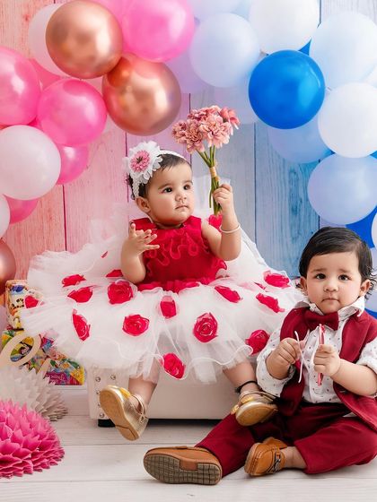 Double the fun with a twins photoshoot! These two little ones are perfectly styled in coordinating red and white outfits against a festive backdrop of balloons.