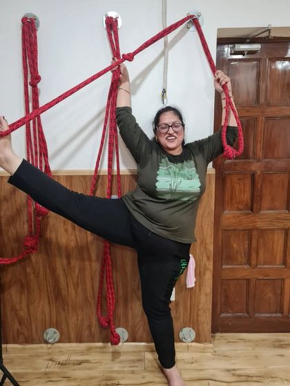 With a smile, this student enjoys the support of the wall ropes to lift her leg higher in a standing split. Props make the practice joyful and accessible.