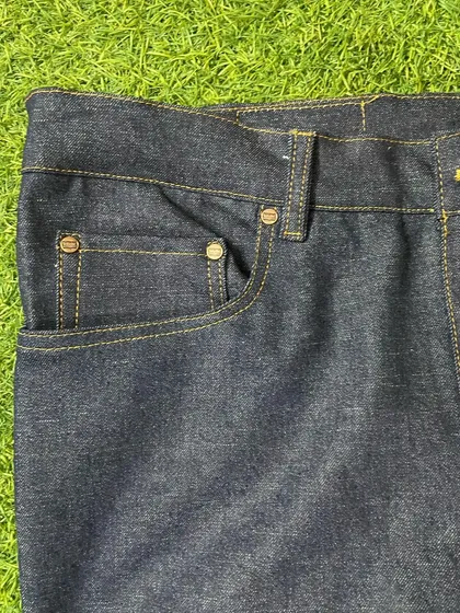 Another look at the front pocket construction, highlighting the quality of the dark denim fabric and the precision of the golden thread stitching.