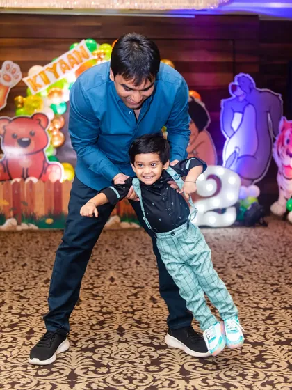 A father playfully swings his son at his second birthday party, a moment of pure fun and connection.