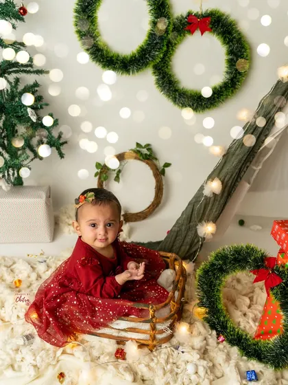 Sitting pretty in her Christmas sleigh. This baby girl is ready for the holidays in a setup complete with wreaths, presents, and a decorated tree.