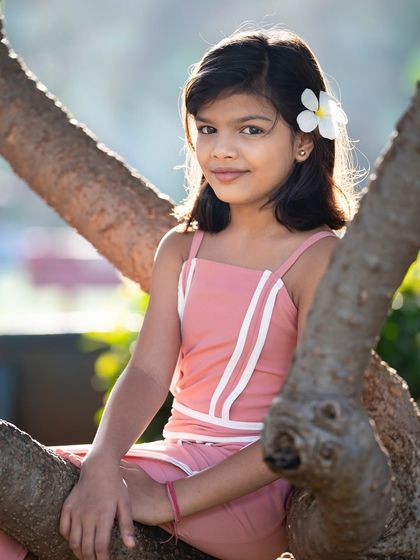 A serene portrait of a girl sitting in a tree, with a flower in her hair. We love finding unique spots in nature that add a touch of magic to our children's photoshoots.