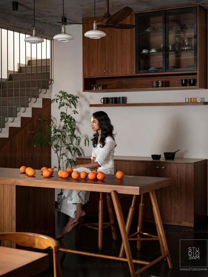 A woman sits at the large wooden breakfast bar, showcasing the kitchen's role as a social hub in the home.