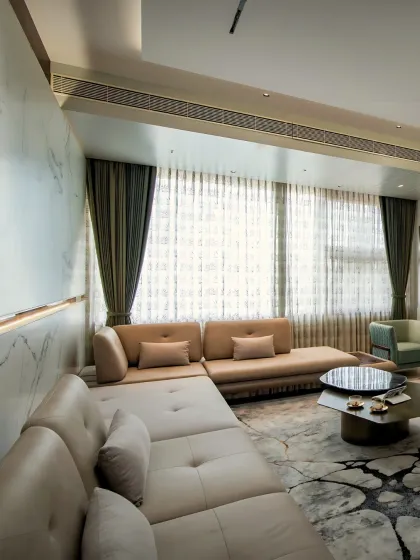 A cozy yet elegant living room corner featuring a custom sectional sofa, layered curtains for light control, and a striking marble-patterned rug. The back-lit marble wall adds a touch of understated luxury and warmth.