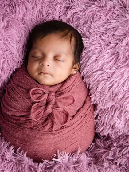 This portrait showcases the 'potato sack' pose with a decorative double bow wrap, set against a rich, textured purple rug.