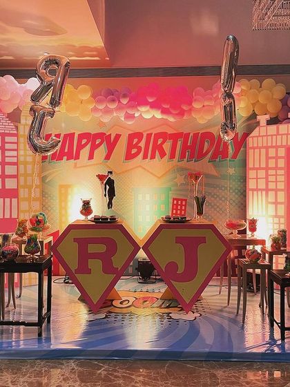 The cake-cutting stage for a twin superhero party. The backdrop features a stylized city skyline, and each girl had her own 'S' logo pedestal for her cake, making them both feel like the hero of the day.
