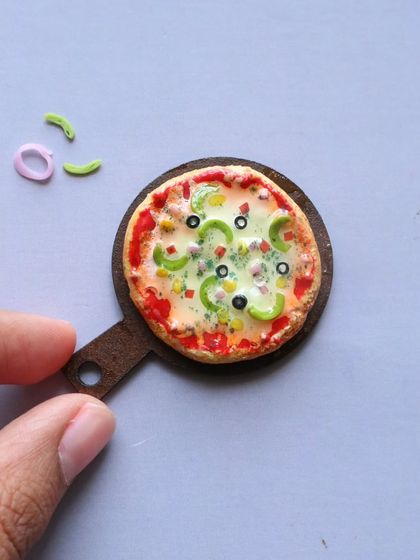 A close-up of a miniature pizza, showing the cheese, olives, and capsicum.