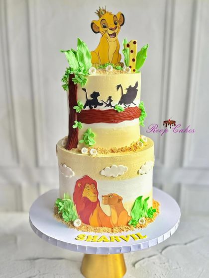 A magnificent two-tier Lion King cake celebrating a little cub's first birthday. The design features beautiful scenes with Simba, Mufasa, and friends, capturing the spirit of the Pride Lands.