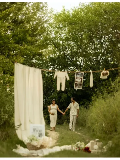 A creative outdoor setup telling the story of what's to come. The couple walks hand-in-hand on a path decorated with a clothesline of baby items, a beautiful way to announce that their baby is on the way.