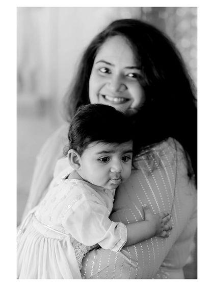 A sweet and intimate black and white portrait of a baby being held. The focus is entirely on the child's innocent and slightly pouty expression.