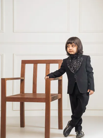 A full length standing view of the black sequin cowl neck tuxedo. The tailored fit and unique neckline make it a standout piece of formal wear for kids.