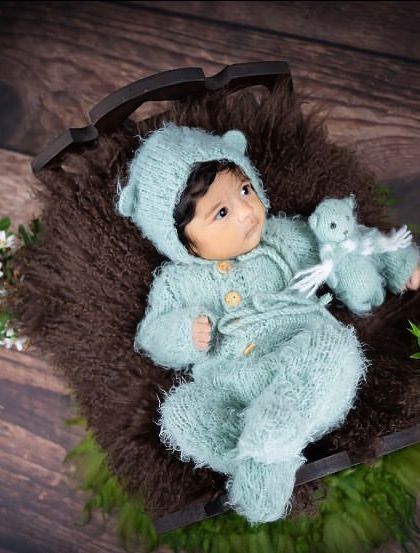 This little one is ready for a teddy bear picnic, dressed in a fuzzy, bear-eared outfit and resting on a miniature bed. It's a sweet and playful theme for a newborn session.
