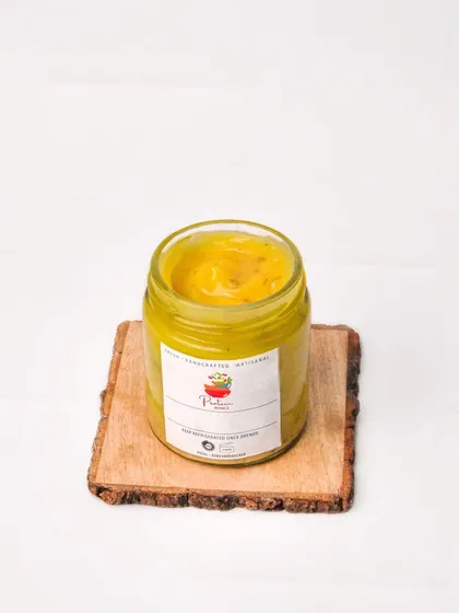 A jar of artisanal yellow dip, possibly a mustard or mango sauce, presented on a rustic wooden slice against a clean white background. This is a great product shot for an indie brand.