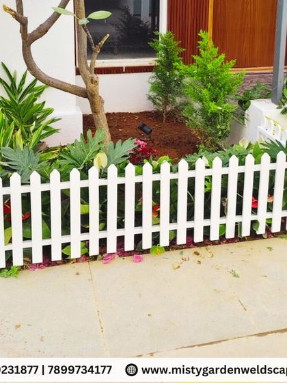 A simple and charming white picket fence encloses a garden bed around a tree, protecting the plants and adding a classic design element to the front yard.