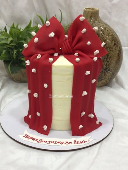 A stylish and elegant cake designed to look like a gift box. This single-tier cake is covered in white ganache and wrapped with a beautiful, hand-sculpted red bow with white floral embossing.