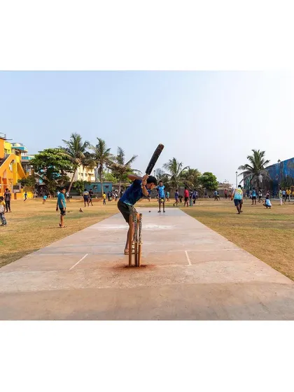 A batsman in action on the cricket pitch at the Worli ground. The design provides a dedicated, level pitch that serves as the centerpiece for the community's most popular sport.