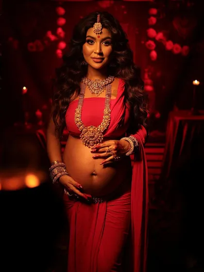Embracing the divine feminine, this traditional maternity portrait is a tribute to our heritage. Dressed in a powerful red and adorned with temple jewelry, the mother-to-be is captured as a symbol of 'Janani', the creator, in a setting filled with cultural richness and strength.