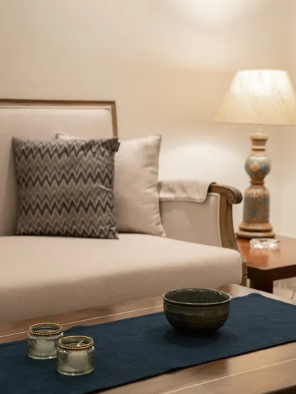 Contrast is a key element of design. Here, a soft, neutral sofa with a chevron-patterned cushion is paired with a rustic ceramic lamp and a deep blue table runner, creating a balanced composition of textures and colors.