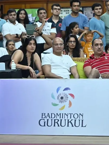 The audience and our team watch a match intently, with Badminton Gurukul branding prominently displayed. We provide end-to-end solutions, including event branding and promotion.
