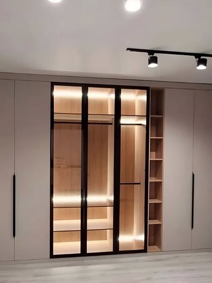 A modern and beautiful closet designed to maximize space and elevate your living area. This wardrobe features a mix of closed cabinets, open side-shelving, and a central glass display with integrated lighting, creating a true showstopper.