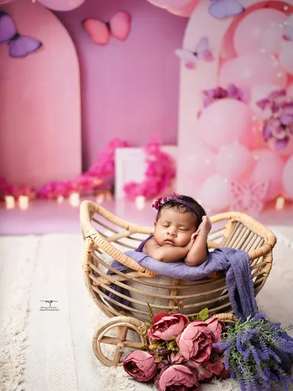 A newborn sleeps peacefully in a wicker pram, surrounded by a dreamy pink and purple butterfly theme. I design each setup to be a beautiful, imaginative world for your baby.