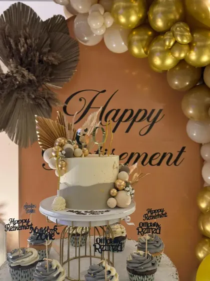 The dessert table was a highlight of the retirement party. It featured a stunning cake and cupcakes that matched the theme, complete with a "Happy Retirement" backdrop and boho-chic dry pampas grass accents.