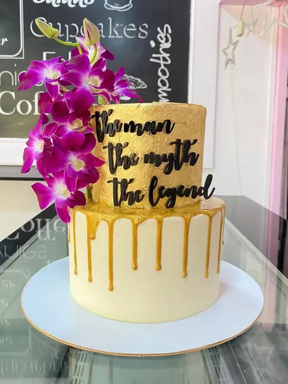 A two-tiered cake for "The Man, The Myth, The Legend." The gold drip and fresh orchids make this a truly legendary centerpiece.