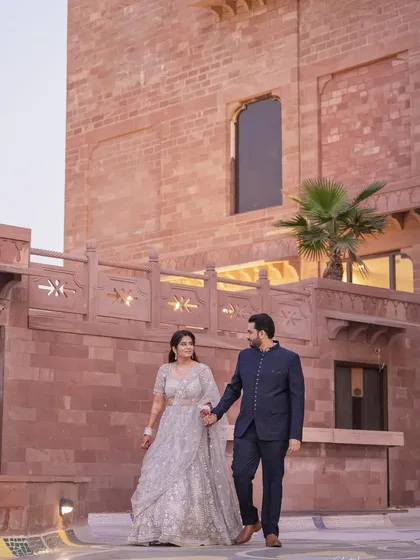 The couple takes a romantic stroll, hand in hand, against the backdrop of a stunning Jodhpur palace. A perfect blend of location and emotion.