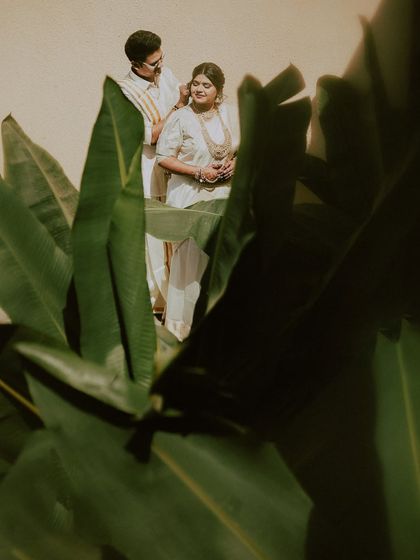 A creative portrait peeking through lush leaves. This framing adds a sense of intimacy and discovery, as if we are getting a private glimpse of the couple's love story.