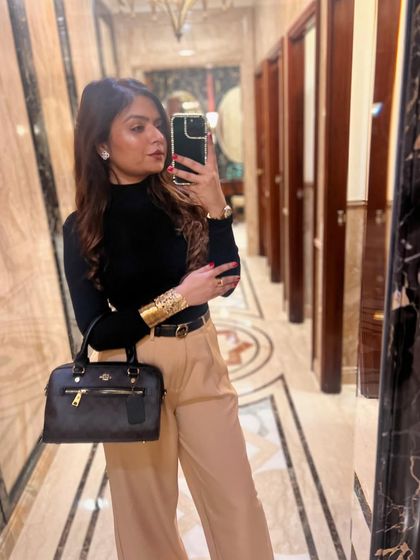 A mirror selfie showcasing a chic winter look with a black turtleneck and beige trousers.