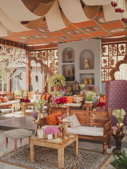 The seating area for the 'Artisan's Studio' Mehendi, featuring layered rugs, carved wooden furniture, and shelves filled with artifacts to create a warm, eclectic vibe.