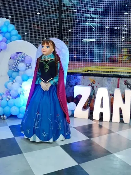 The Anna mascot stands ready to greet guests at a 'Frozen' party, with the birthday girl's name lit up in the background.