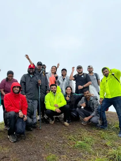 A small group in high spirits, posing in their rain gear on a grassy slope during a monsoon trek.